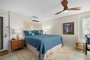 Une chambre à coucher avec un lit, des tables de chevet, un ventilateur de plafond, un tableau et une porte.