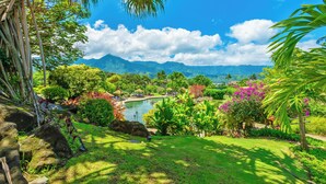 A lush garden with a pond, palm trees, and a view of distant mountains. - (4102/03) 2Br Ground Floor Hanalei Bay Resort, Ocean View, Pool, Tennis (Princeville)