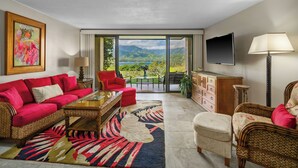 A spacious living room with a red sofa, a coffee table, and a view of mountains and a lake through large glass doors. - (4102/03) 2Br Ground Floor Hanalei Bay Resort, Ocean View, Pool, Tennis (Princeville)