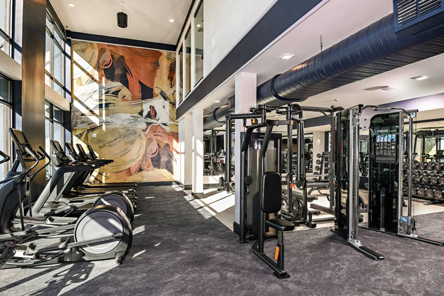 Une salle de sport équipée de machines de cardio, de machines de musculation et ornée d’une grande fresque murale.
