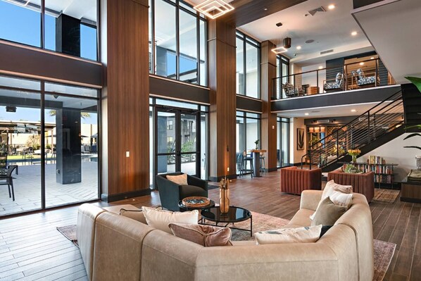 A spacious indoor area with a high ceiling, large windows, and a staircase leading to an upper level.