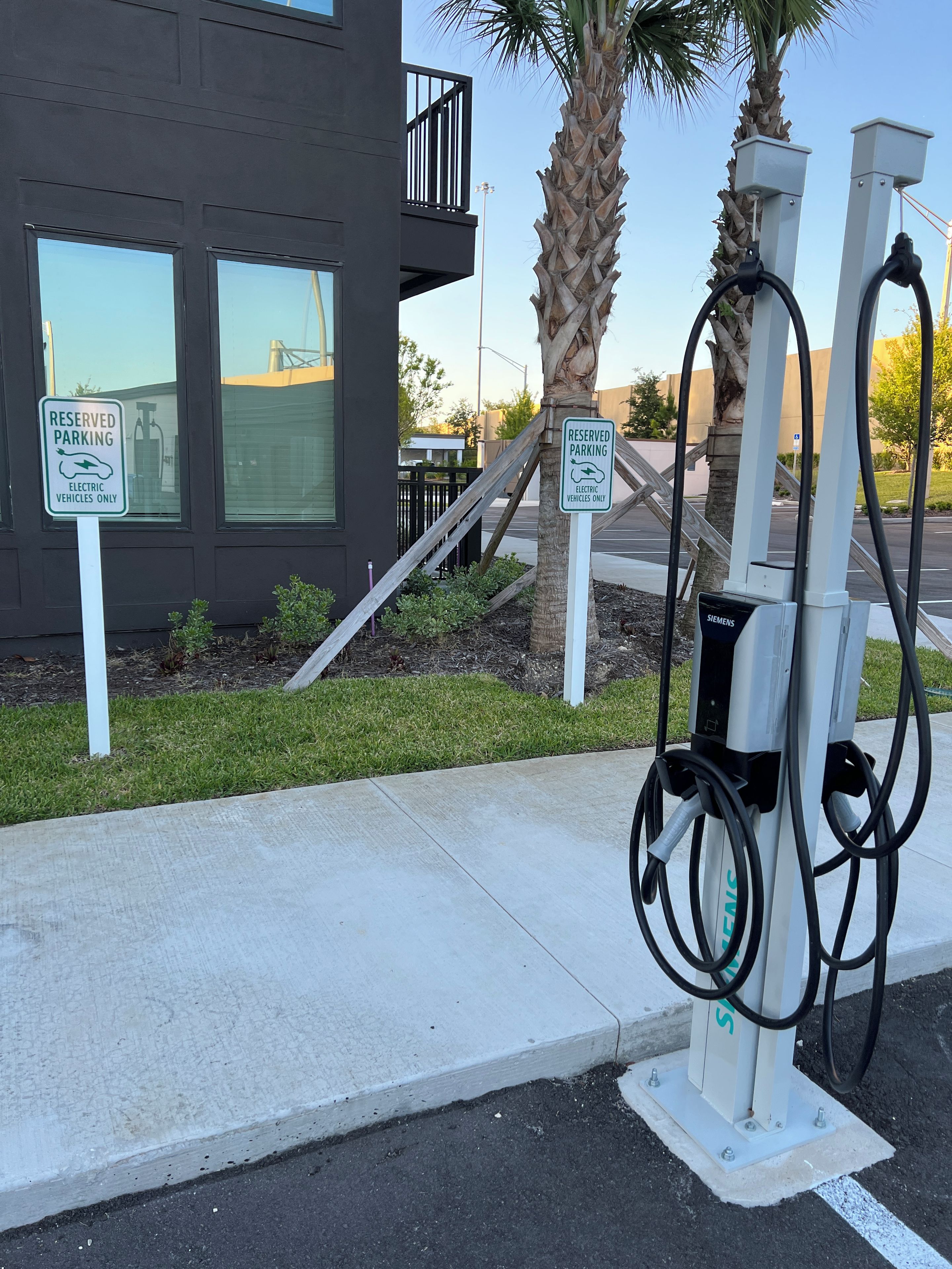A parking area with electric vehicle charging stations, a reserved parking sign, and a modern building in the background.