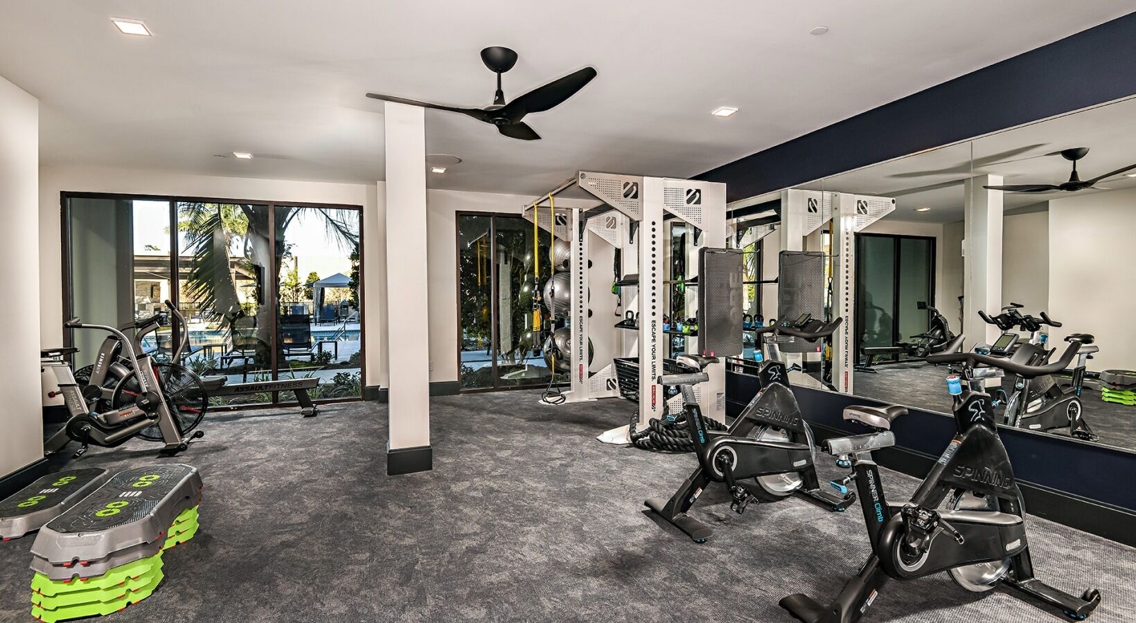 A gym with various exercise equipment, large windows, and a ceiling fan.