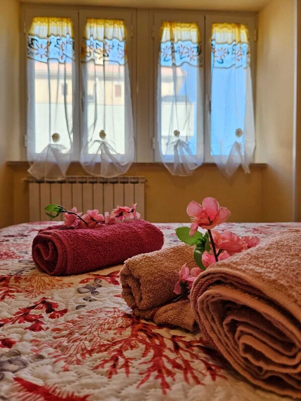 A hotel room with a bed, rolled towels, and a radiator.