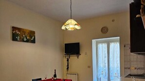 Un coin repas avec une table dressée pour deux personnes, un téléviseur fixé au mur et un espace cuisine équipé d’un évier et d’un plan de travail.