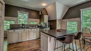 Une cuisine avec des meubles en bois, un îlot central et une vue sur les arbres grâce à de grandes fenêtres.