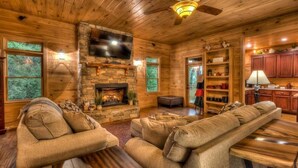 L’intérieur d’un chalet confortable, avec des murs en rondins de bois, une cheminée en pierre, des meubles en bois et un coin cuisine.