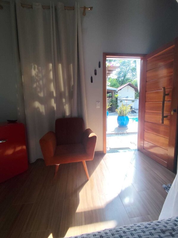 Una habitación con piso de madera, una silla roja, una puerta de madera y vistas al exterior.