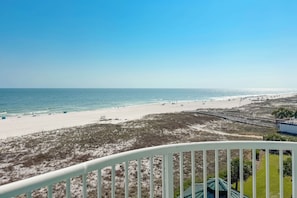 A beach view from a balcony with a railing, sandy beach, and ocean.