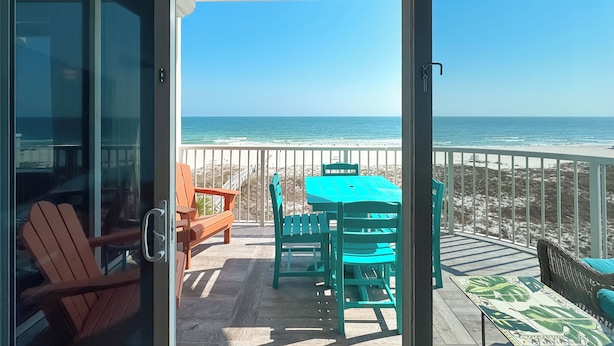 A balcony with a view of the ocean, a table with chairs, and a wooden chair. - Spanish Key 407 | Steps from Flora Bama | Pools, Hot Tub, Gym & More! | My Beach Getaways (Pensacola)