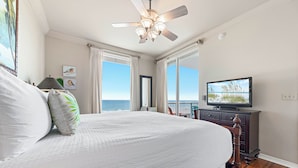 A bedroom with a large bed, a ceiling fan, a television, and a view of the ocean. - Spanish Key 407 | Steps from Flora Bama | Pools, Hot Tub, Gym & More! | My Beach Getaways (Pensacola)