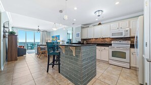 A modern kitchen with white cabinets, a built-in island, and a large window. - Spanish Key 407 | Steps from Flora Bama | Pools, Hot Tub, Gym & More! | My Beach Getaways (Pensacola)