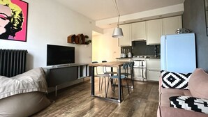 Ein modernes Wohnzimmer mit Esstisch aus Holz, einem Fernseher und einer Küche im Hintergrund.