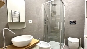 Ein modernes Badezimmer mit einer Duschkabine, einem weißen Waschbecken und einer Toilette.