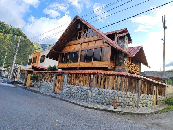 Ein zweigeschossiges Holzhaus mit großen Fenstern, einem Steinfundament und einem roten Ziegeldach.
