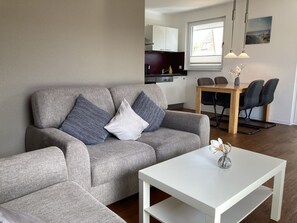 Una sala de estar moderna con un sofá gris, una mesa de centro blanca y una zona de comedor con una mesa y sillas de madera.