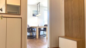 Een moderne kamer met een houten garderobe, een bureau met stoelen en uitzicht op een andere kamer met een tafel en stoelen.