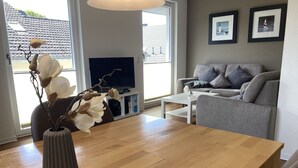 Een moderne woonkamer met een houten eettafel, een grijze bank en een televisie op een standaard.