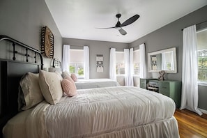 A bedroom with a bed, a ceiling fan, a dresser, and a window with curtains.