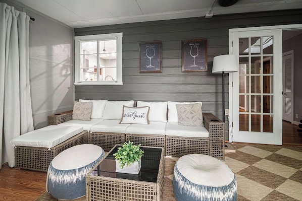 A cozy living area with a sofa set, two round ottomans, a coffee table with a plant, and framed wine glasses on the wall.