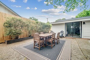 A patio with a wooden table and chairs, a black rug, and a wooden fence.