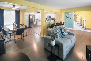 A spacious living area with a dining table, chairs, a sofa, and a kitchen in the background. -  Modern 6BR West Omaha, 2-Car Garage, W/D, Smart TV, Pet-Friendly, 1 Gbps (Omaha)