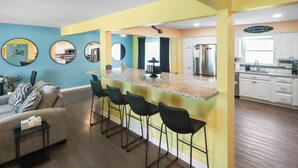 Una cocina moderna con una isla central, taburetes de bar y una zona de comedor con sofá y sillas.