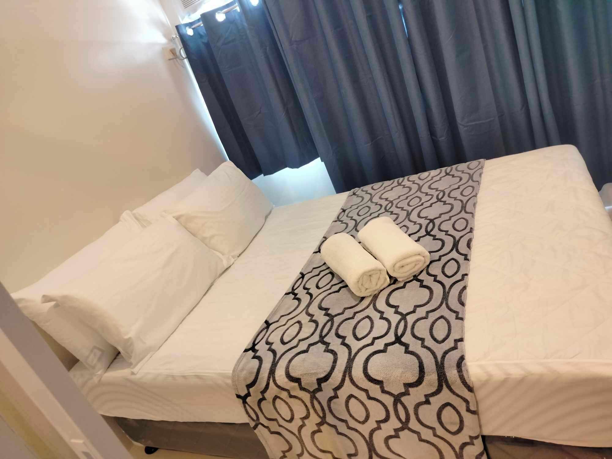 Une chambre d’hôtel avec un lit, du linge de lit blanc, une couvre-lit à motifs et une fenêtre avec des rideaux.