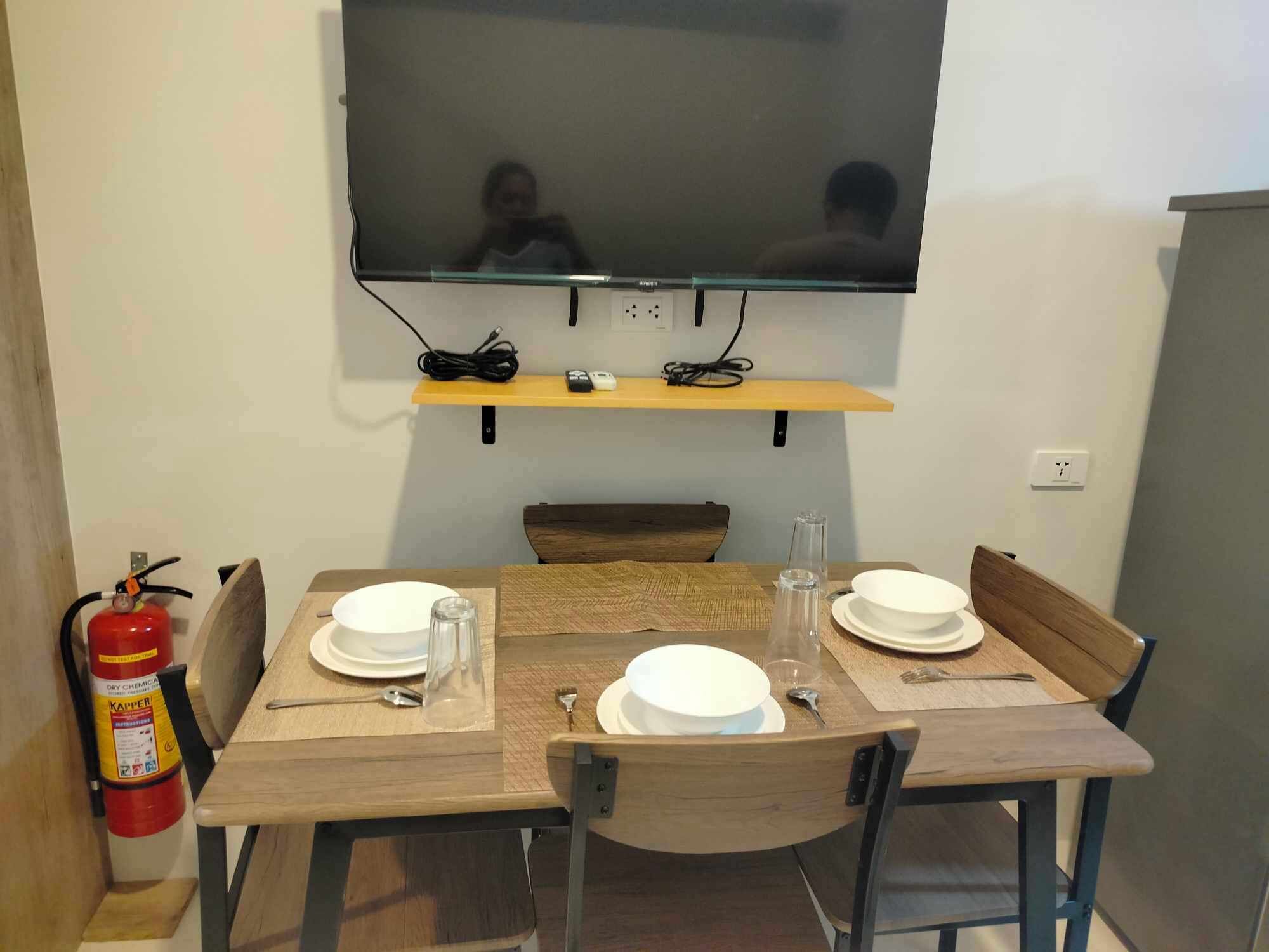 Un comedor con una mesa lista para dos, un televisor montado arriba y un extintor a la izquierda.