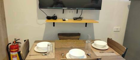 Un comedor con una mesa lista para dos, un televisor montado arriba y un extintor a la izquierda.
