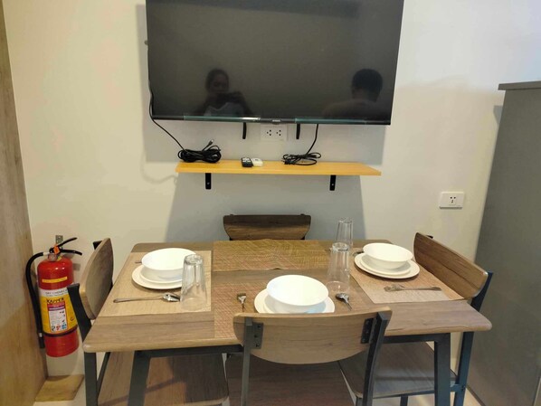A dining area with a table set for two, a mounted TV above, and a fire extinguisher to the left. - Prime World District (Lapu-Lapu)