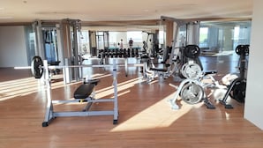 A spacious gym with various exercise equipment, large windows, and a wooden floor.