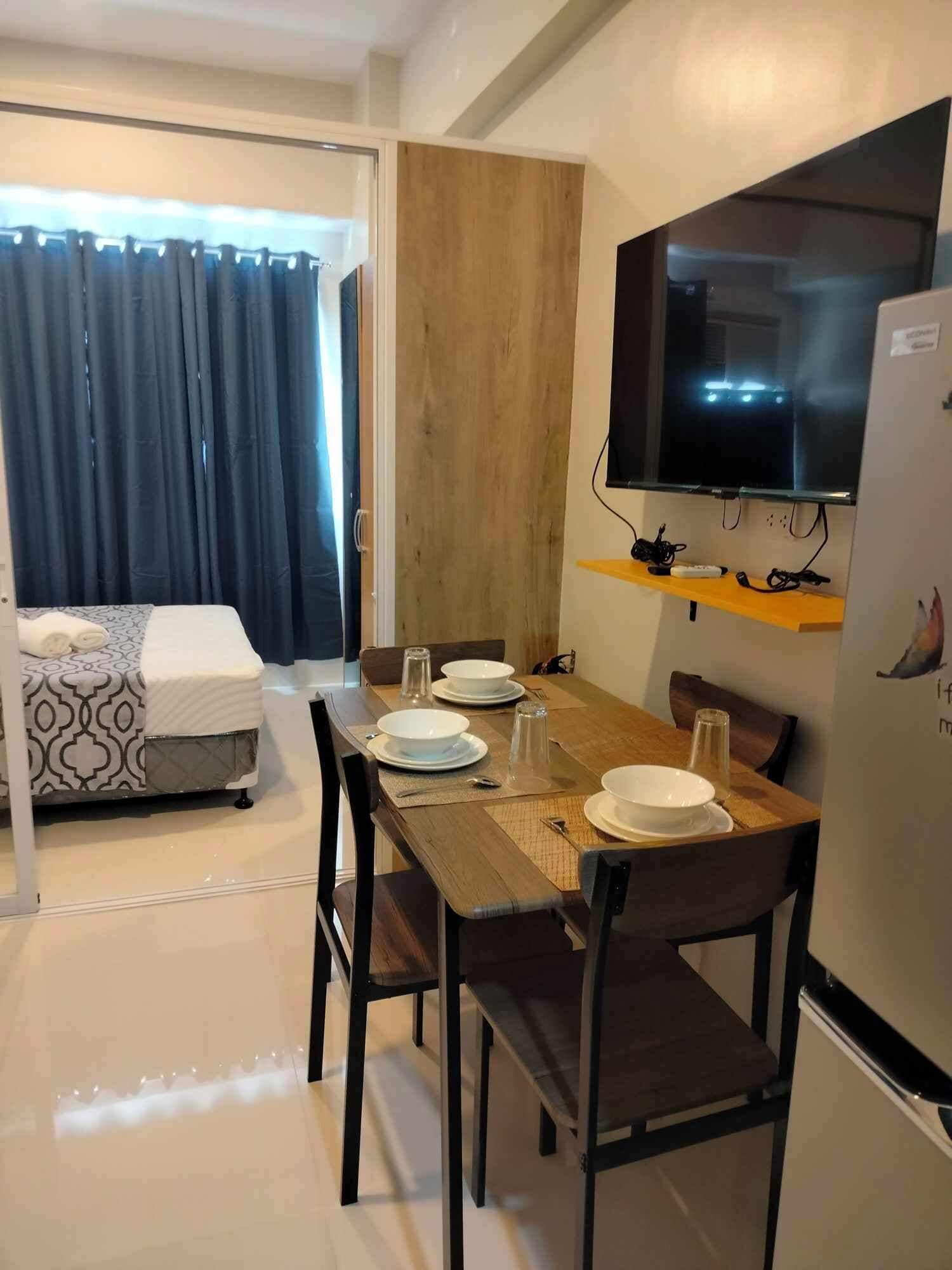 A compact hotel room with a dining area, a bed, a TV, and a wooden wall.