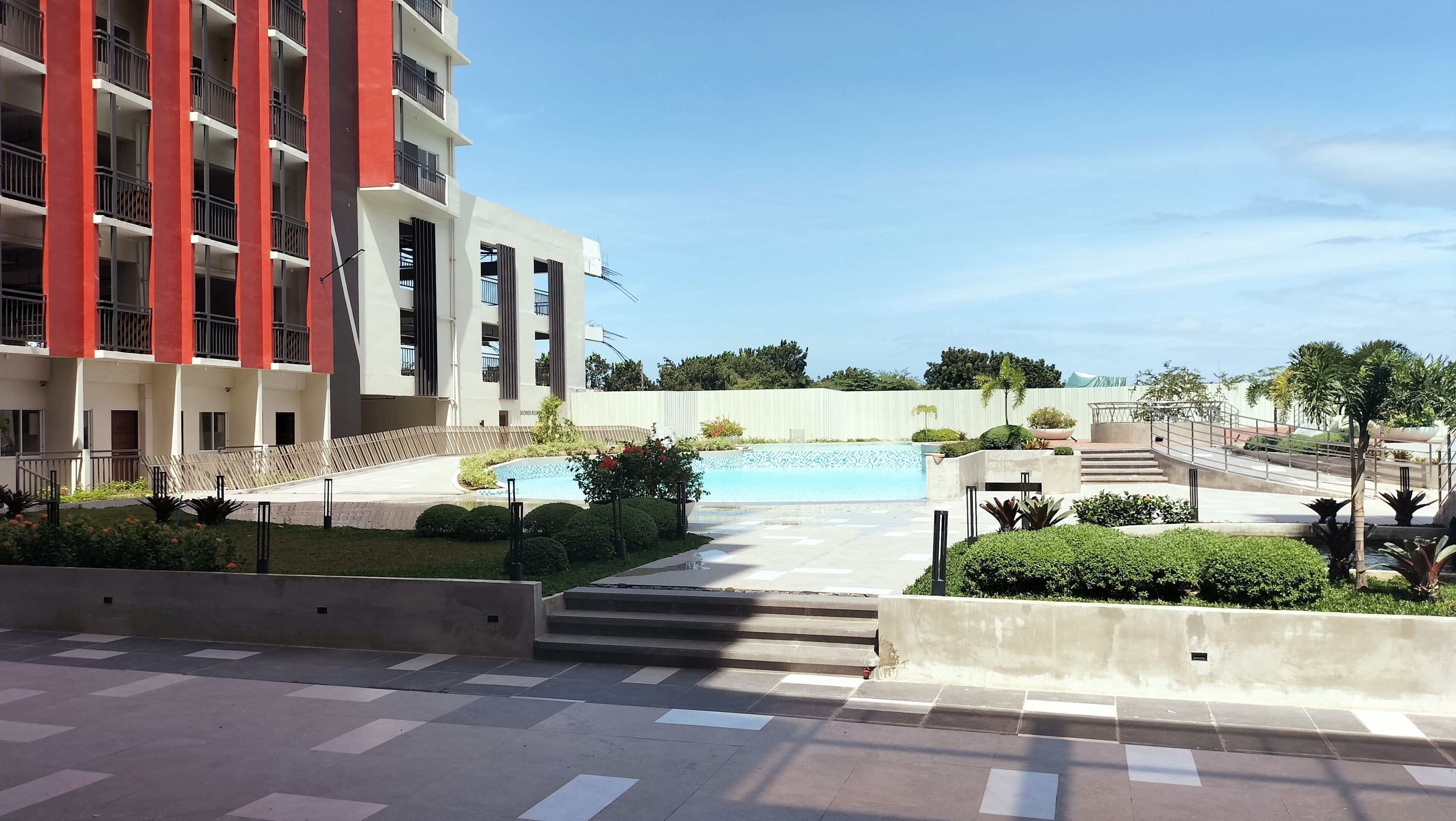 A modern building with a swimming pool, surrounded by well-maintained gardens and a clear sky.
