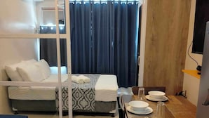 A compact hotel room with a bed, a dining table with chairs, and a TV.