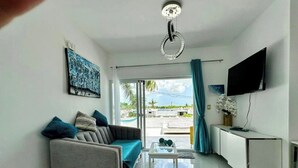 Una sala de estar moderna con un sofá gris, una mesa de centro, un televisor y vistas al exterior.