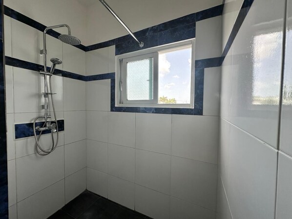 A bathroom with white tiles, a shower, and a window.
