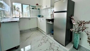 Una cocina moderna con gabinetes blancos, un refrigerador de acero inoxidable y piso de mármol.