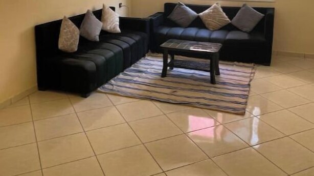 A living room with a black sectional sofa, a coffee table, and a patterned rug. - Takdoum a Coté Merjan Market (Beni melalle)