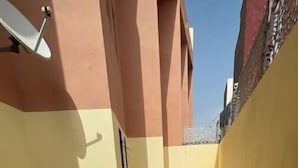 A narrow tiled corridor with yellow and pink walls, a satellite dish, and a shadow pattern on the floor. - Takdoum a Coté Merjan Market (Beni melalle)