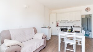 A modern kitchen with white cabinets, a dining table with chairs, and a sofa with cushions.
