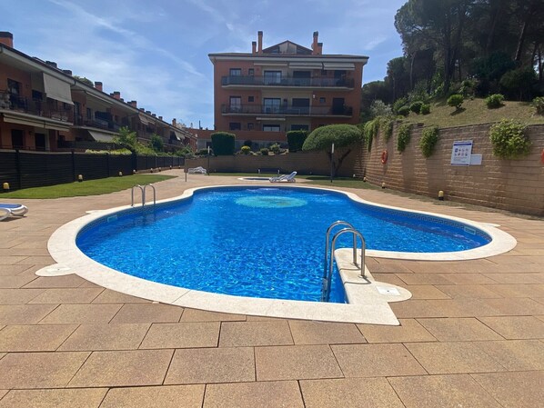 Una piscina con bordo piastrellato, una postazione di salvataggio e un edificio sullo sfondo.