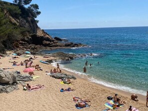 Una spiaggia con persone che prendono il sole e nuotano, scogliere rocciose e acqua cristallina.