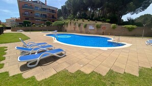 Une piscine avec des chaises longues, un mur de briques et un bâtiment en arrière-plan.