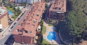 A high-rise building with multiple balconies, a swimming pool, and a road in the foreground.