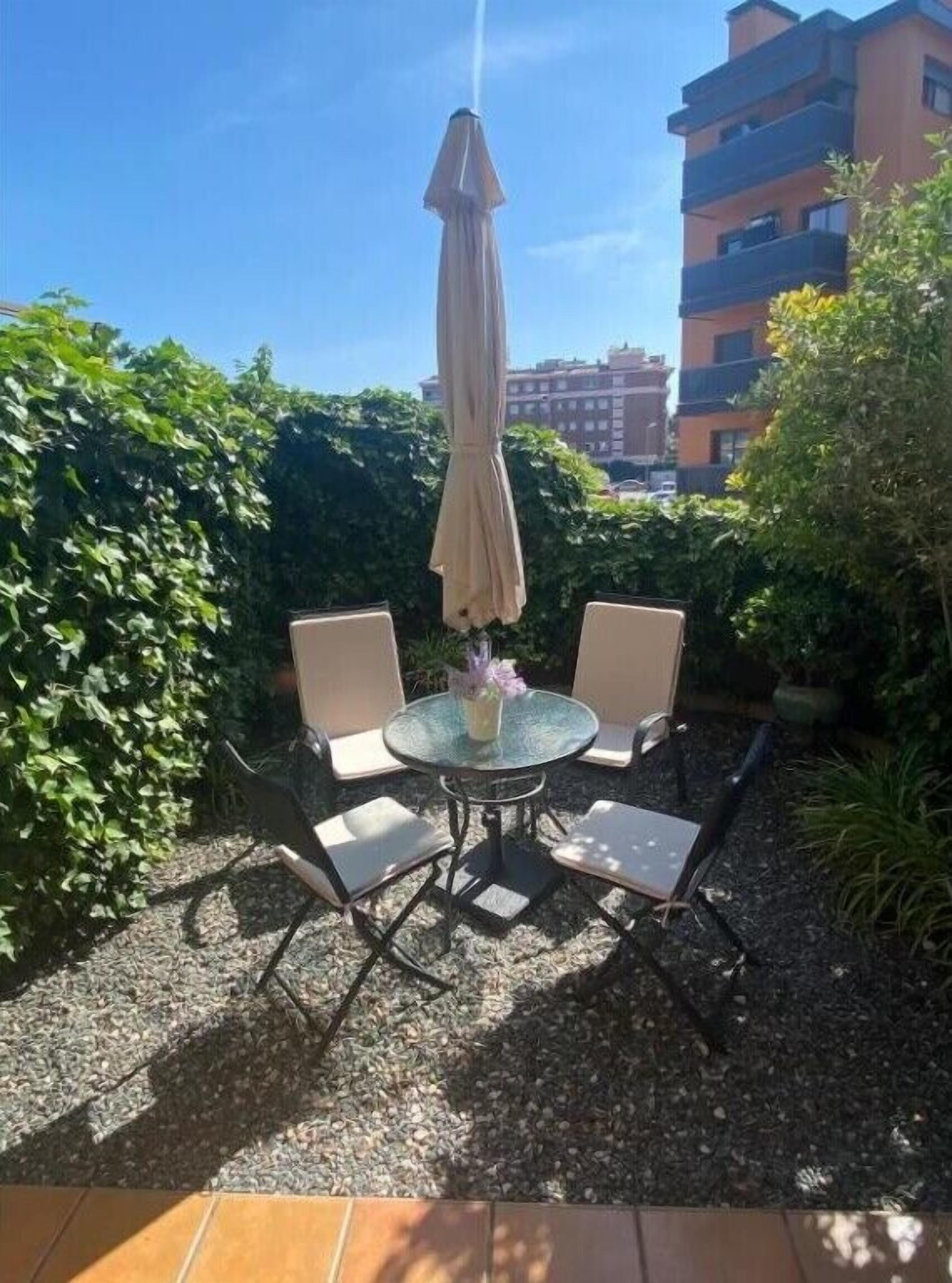 Un patio al aire libre con una mesa redonda, dos sillas y un parasol colgante.