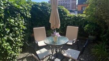 Un patio al aire libre con una mesa redonda, dos sillas y un parasol colgante.