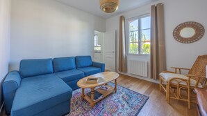 A living room with a blue sofa, a wooden coffee table, a wicker chair, and a patterned rug. - La Maison du Fleuve - Welkeys (Dives-sur-Mer)