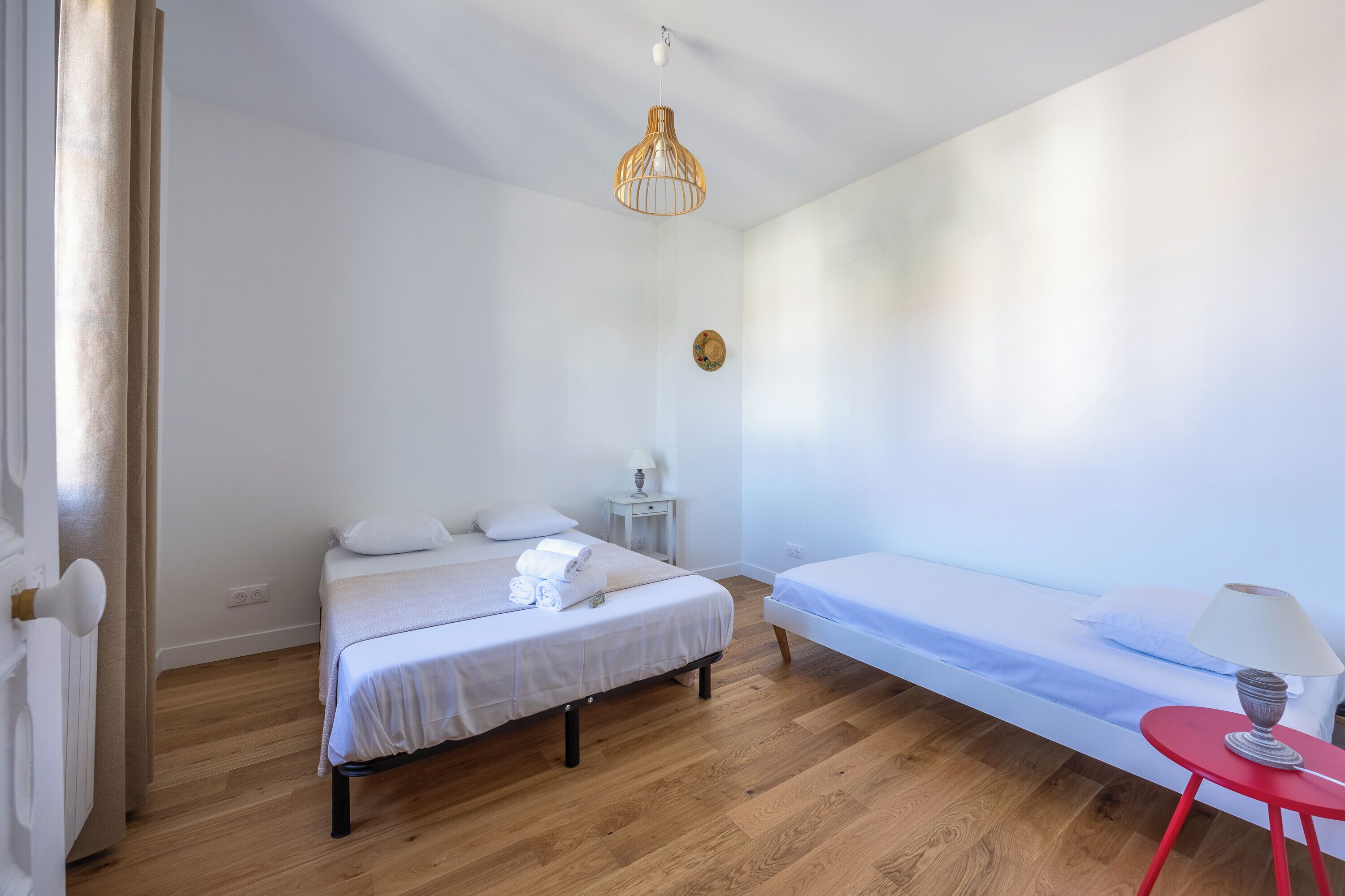 Ein Schlafzimmer mit einem Bett, einem zusätzlichen Bett, einem Nachttisch, einem roten Hocker und einer Pendelleuchte.