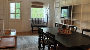 A dining area with a dark wooden table, black chairs, and a television on a white shelf.